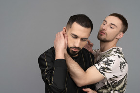 Joven caucásico sosteniendo a otro hombre sensualmente por el cuello en un medio abrazo
