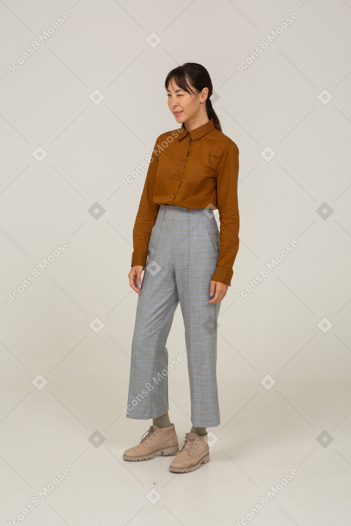 ブリーチとブラウスでウィンクしている若いアジアの女性の4分の3のビュー