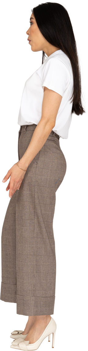 脇を見ながら立っているブリーチとtシャツで驚いた若い女性の側面図