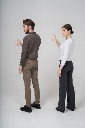 Okサインを示しているオフィス服の若いカップルの4分の3の背面図