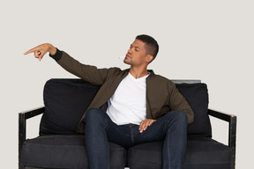 ソファに座って、口の中でタバコを保持している若い傲慢な男の正面図