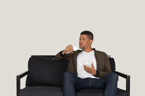 コーヒーを飲みながらソファに座って夢見る若い男の正面図